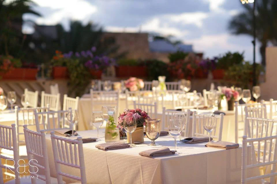 White wedding tables set on the rooftop terrace at sunset, with pink flowers and candles