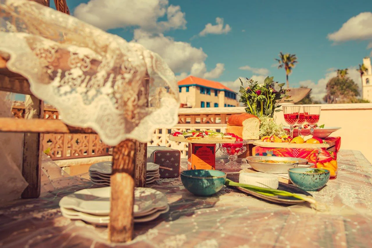 Beautifully styled table outdoors with lace cloth, candles and bread, with Jaffa rooftops in the background